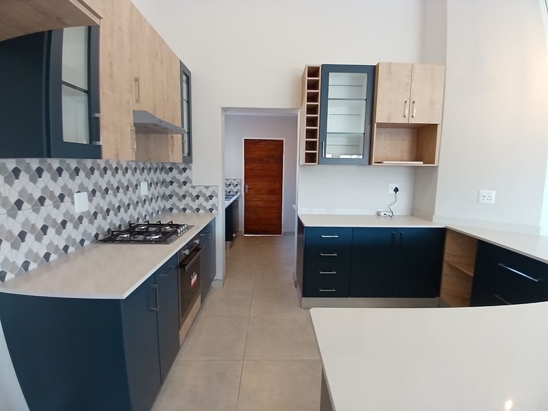 Modern kitchen featuring two-tone cabinetry, stone countertops, a gas hob, built-in oven, and a decorative tiled backsplash with neutral floor tiles.