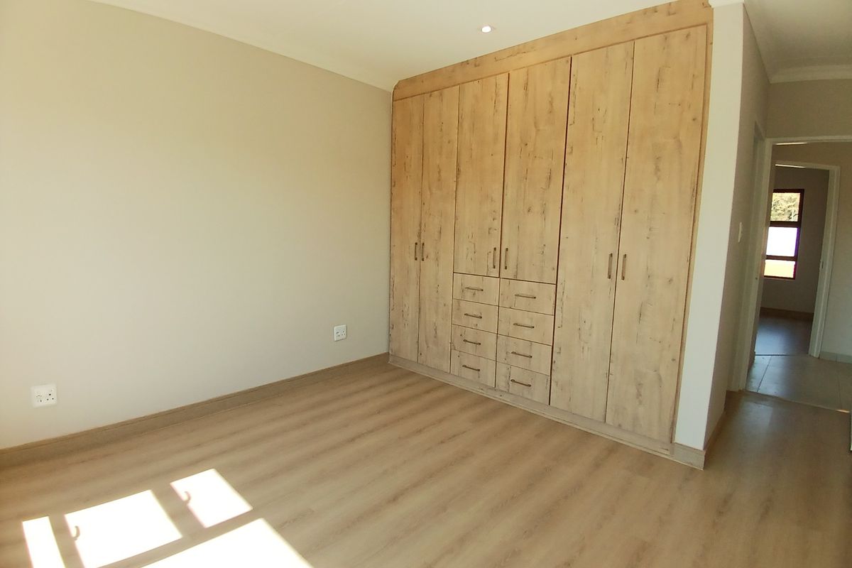 A bright, empty bedroom featuring modern light wood-look laminate flooring and extensive built-in cupboards with integrated drawers.