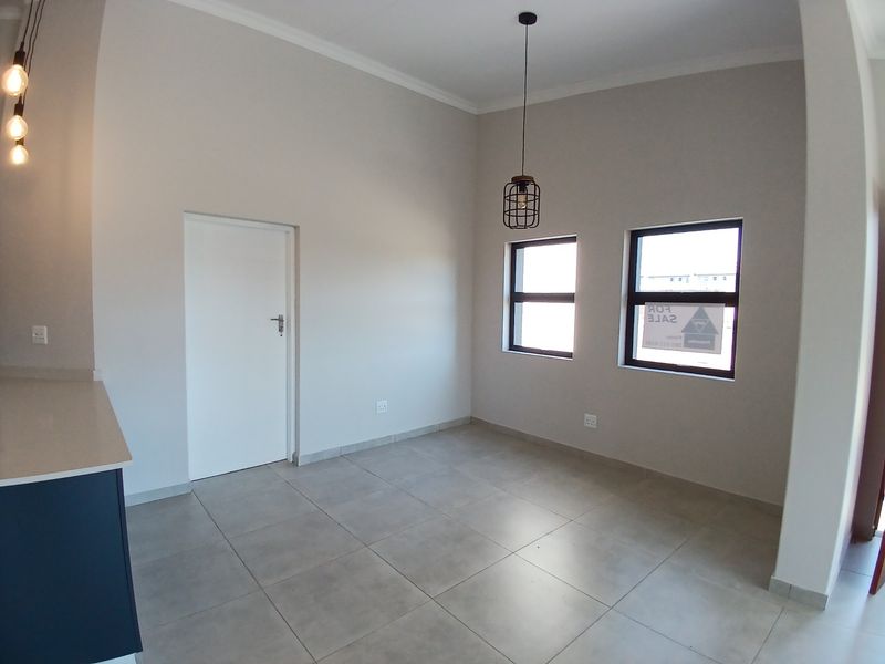 An open-plan living area featuring neutral tiled flooring, modern pendant lighting, and a partial view of a kitchen with stone countertops.