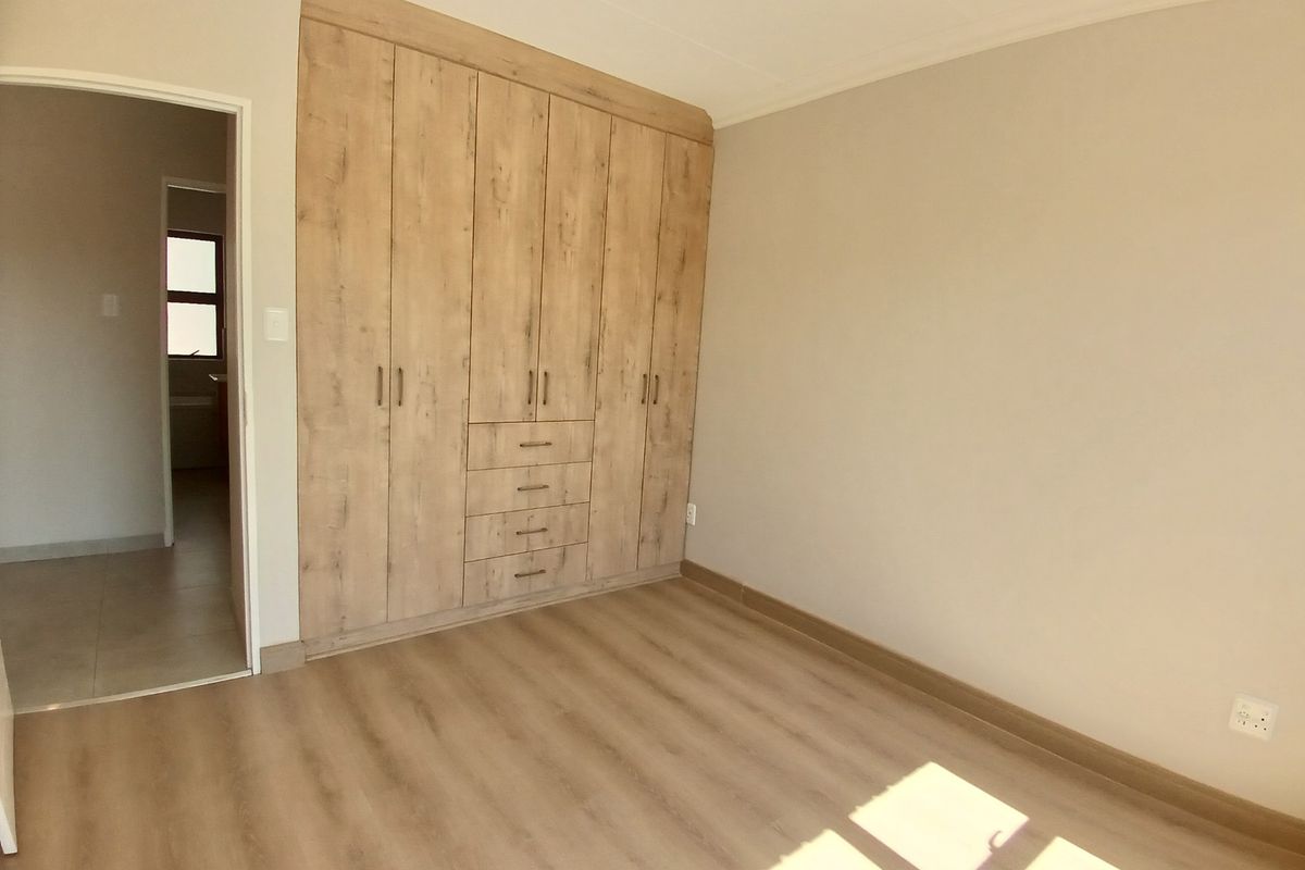 A bright, empty bedroom featuring modern wood-look built-in cupboards and light laminate flooring, offering a clean and neutral space ready for personalization.