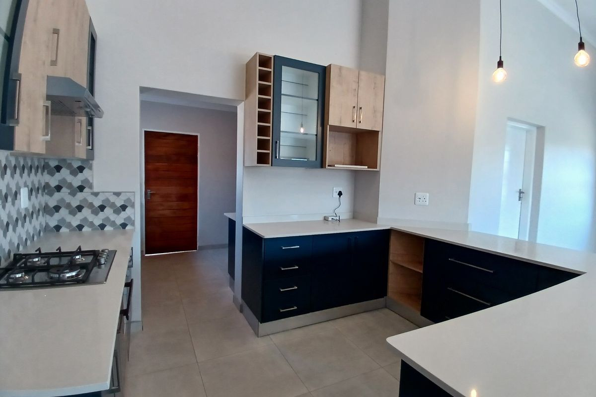 Modern kitchen featuring two-tone cabinetry, stone countertops, gas hob, extractor fan, and stylish tiled backsplash in an open-plan layout.