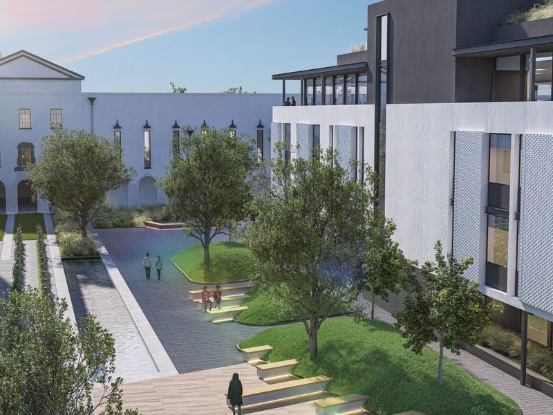 A modern office courtyard featuring landscaped green spaces, paved walkways, built-in seating, and a water feature between building wings.
