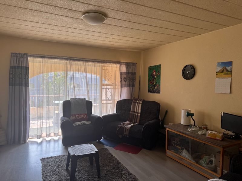 A living room featuring laminate flooring, a textured ceiling, and a large sliding glass door providing access to an outdoor balcony area.