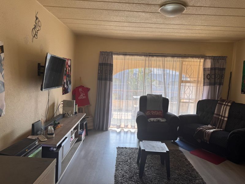 A living room featuring laminate flooring, a textured ceiling, and a sliding glass door leading to a balcony with security gate.