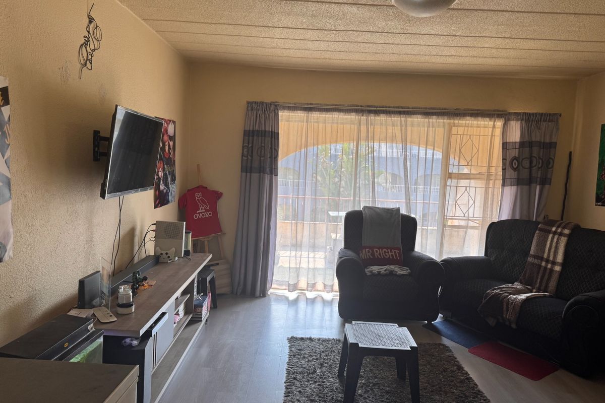 A living room featuring laminate flooring, a textured ceiling, and a sliding glass door leading to a balcony with security gate.