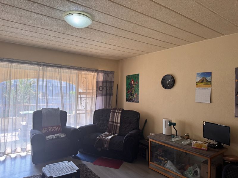 A living room featuring laminate flooring, a flush mount ceiling light, and a large sliding glass door with an integrated security gate.