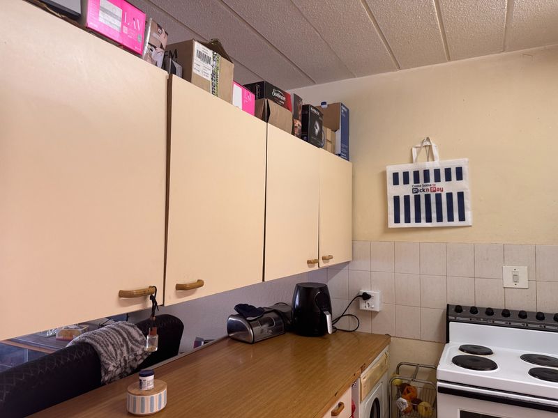 A compact kitchen featuring dated cabinetry, laminate countertops, a tiled backsplash, and a freestanding electric stove.