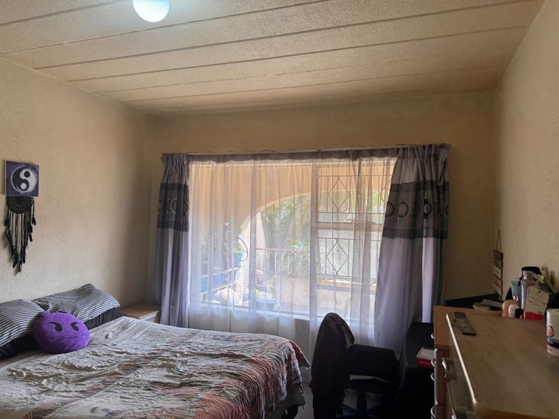 A bedroom featuring a large window with security gate and textured ceiling, requiring cosmetic updates to improve the overall condition of the space.