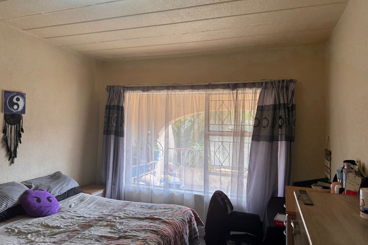 A bedroom featuring a large window with security gate and textured ceiling, requiring cosmetic updates to improve the overall condition of the space.