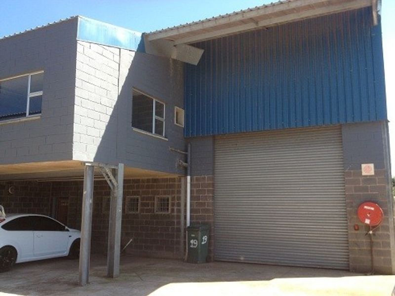 Industrial property exterior featuring a large roller shutter door, corrugated metal cladding, and a covered parking area with concrete block construction.