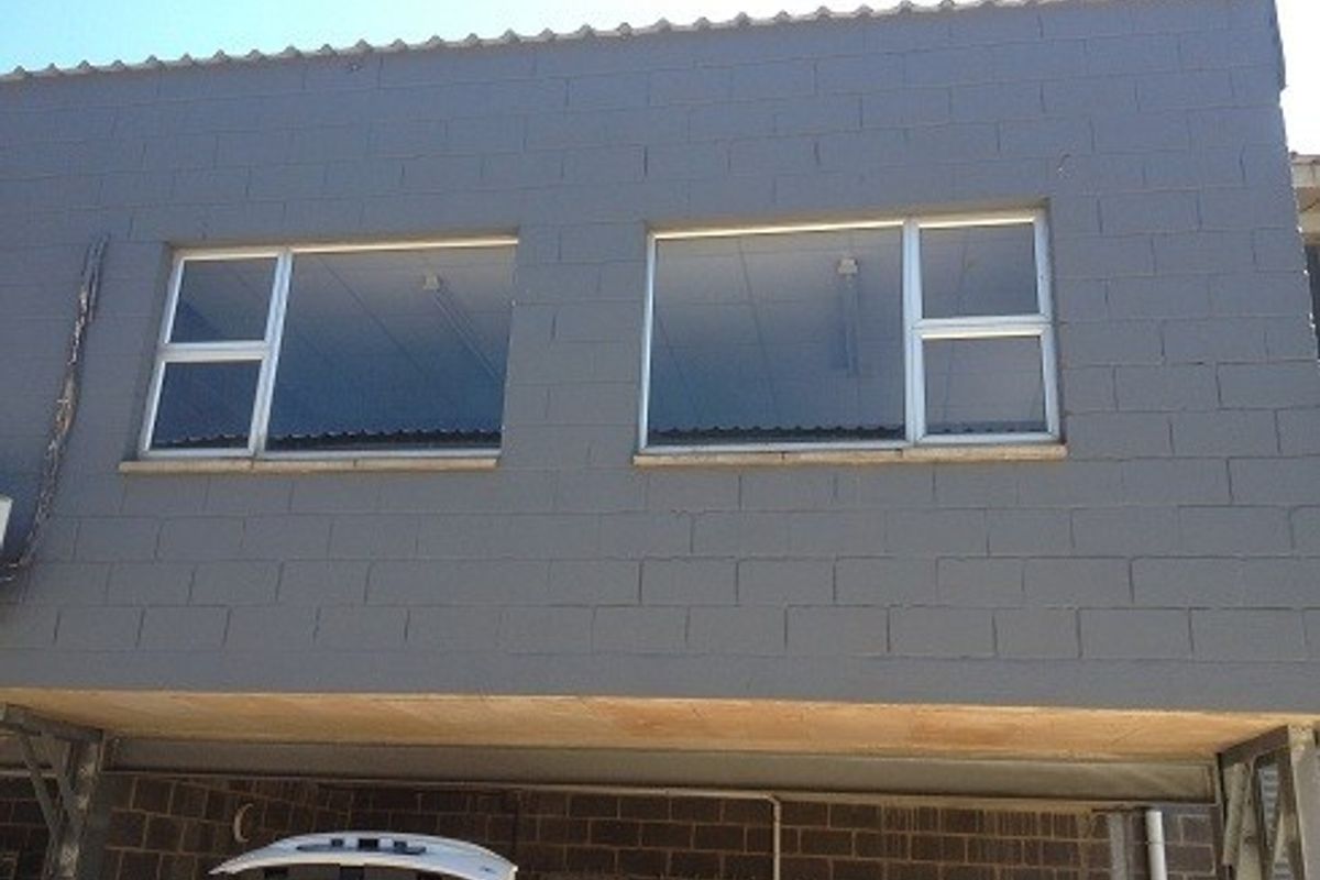 Exterior view of an industrial building featuring a painted concrete block facade with aluminium framed windows and a covered ground level area.