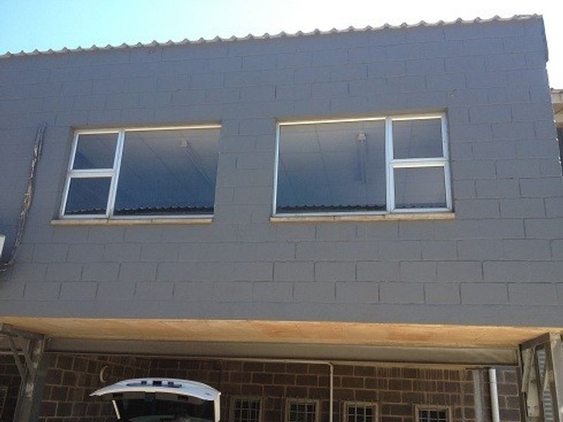 Exterior view of an industrial building featuring a painted concrete block facade with aluminium framed windows and a covered ground level area.