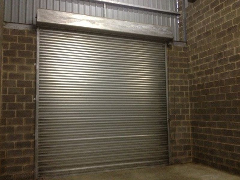 Industrial garage space featuring a secure metal roller shutter door and exposed brick walls.