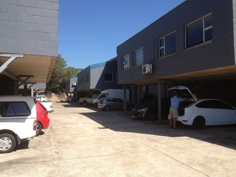 Exterior view of an industrial property featuring a concrete driveway and covered parking bays beneath the building structure.