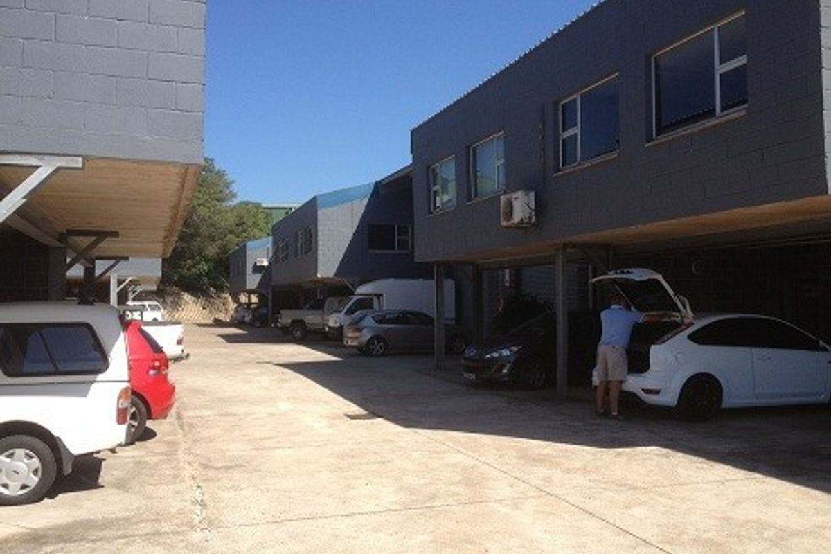 Exterior view of an industrial property featuring a concrete driveway and covered parking bays beneath the building structure.