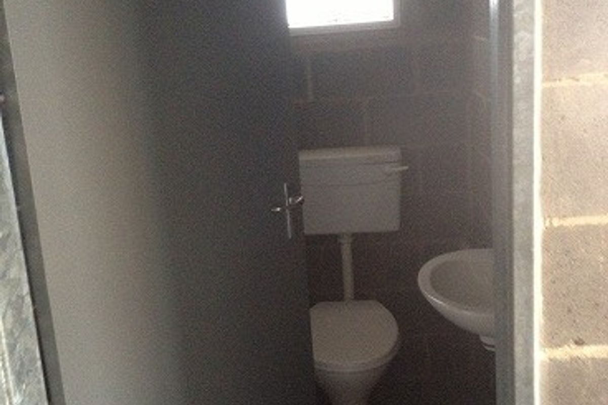 A compact industrial-style bathroom featuring a toilet, wall-mounted washbasin, and exposed brick walls with a small window.