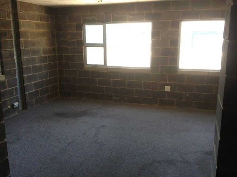 An empty utility space featuring exposed concrete block walls, carpet flooring, and aluminium frame windows, suitable for storage or workshop use.