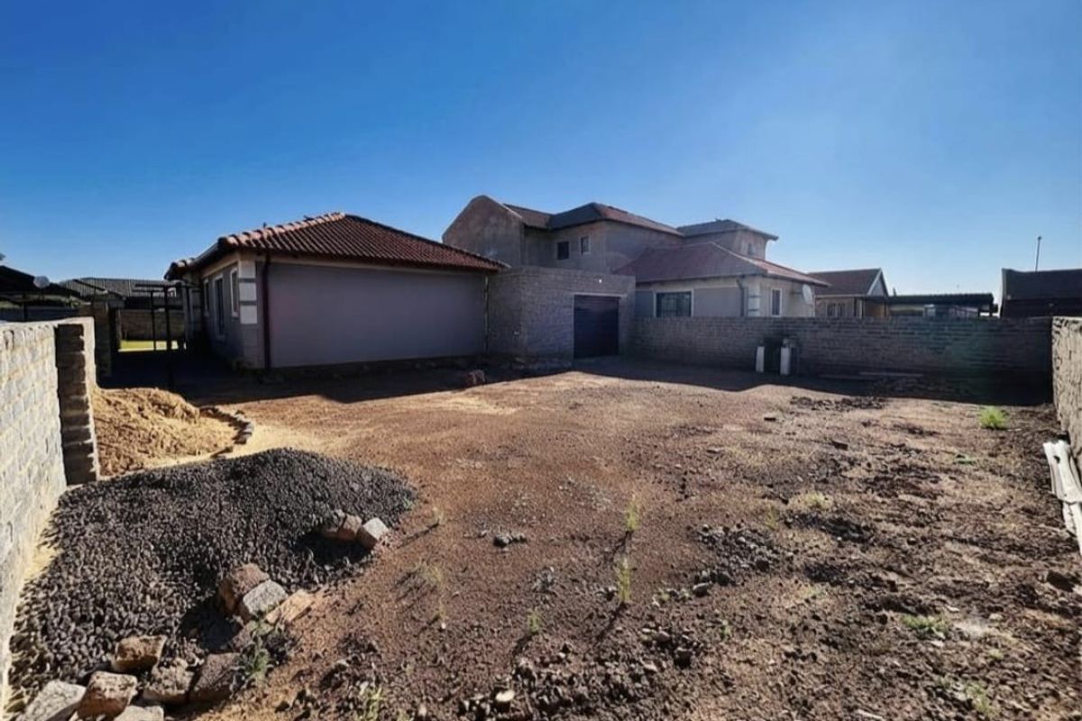 Rear exterior view of the property featuring a large, unlandscaped yard area enclosed by brick boundary walls and a tiled roof structure.