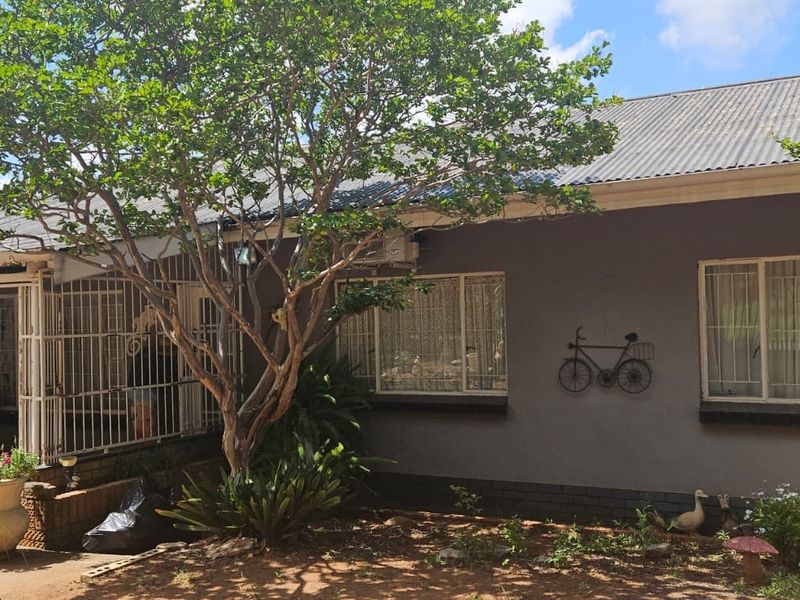 Front elevation of a single-story house featuring a corrugated metal roof, security bars on windows, and a covered patio area.