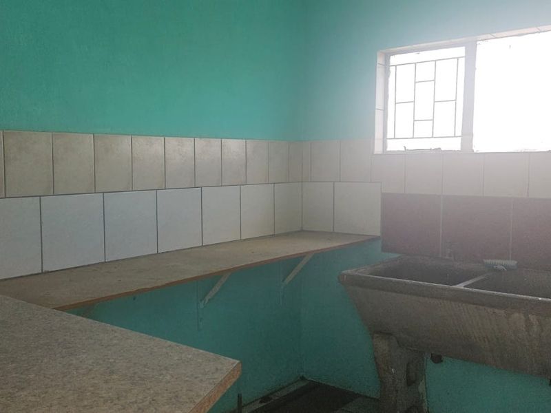 A functional laundry area featuring a concrete double wash trough, laminate work surfaces, and tiled splashbacks, ready for modernization.