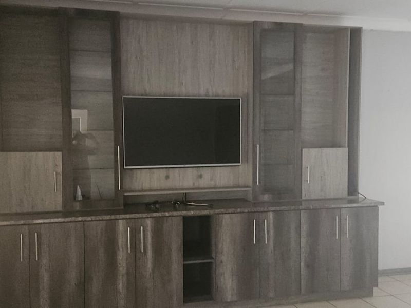 A living room featuring extensive built-in wooden cabinetry with integrated shelving and storage, complemented by tiled flooring and neutral wall finishes.
