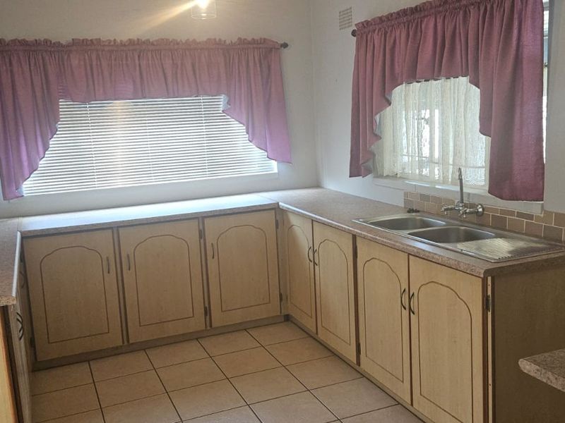 A functional kitchen featuring laminate cabinetry, double bowl sink, tiled splashback, and ceramic tile flooring, offering potential for modern renovation.