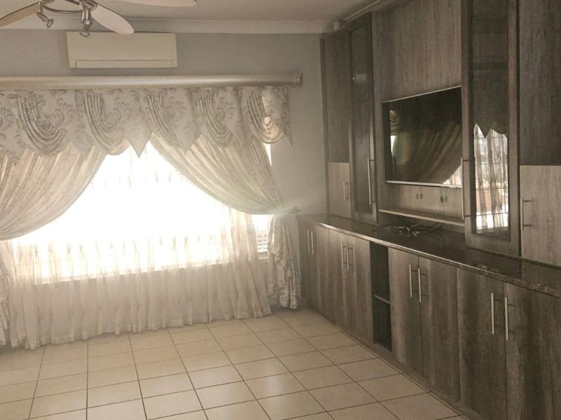 A living room featuring extensive built-in cabinetry, tiled flooring, a ceiling fan, and a wall-mounted air conditioning unit.