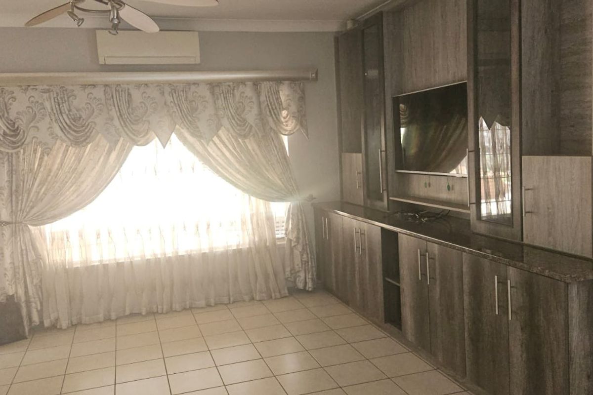A living room featuring extensive built-in cabinetry, tiled flooring, a ceiling fan, and a wall-mounted air conditioning unit.