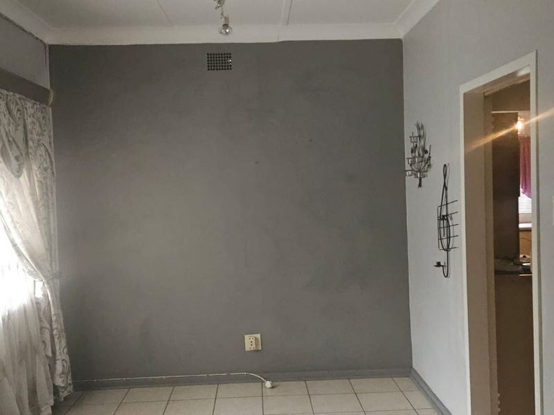 An empty living room featuring tiled flooring, a coved ceiling, and a neutral grey accent wall, offering a blank canvas for interior design.