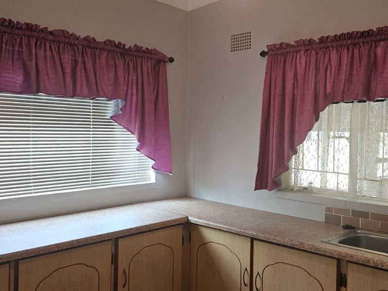 A functional kitchen area featuring laminate countertops, built-in cabinetry, and a stainless steel double sink with a tiled splashback.