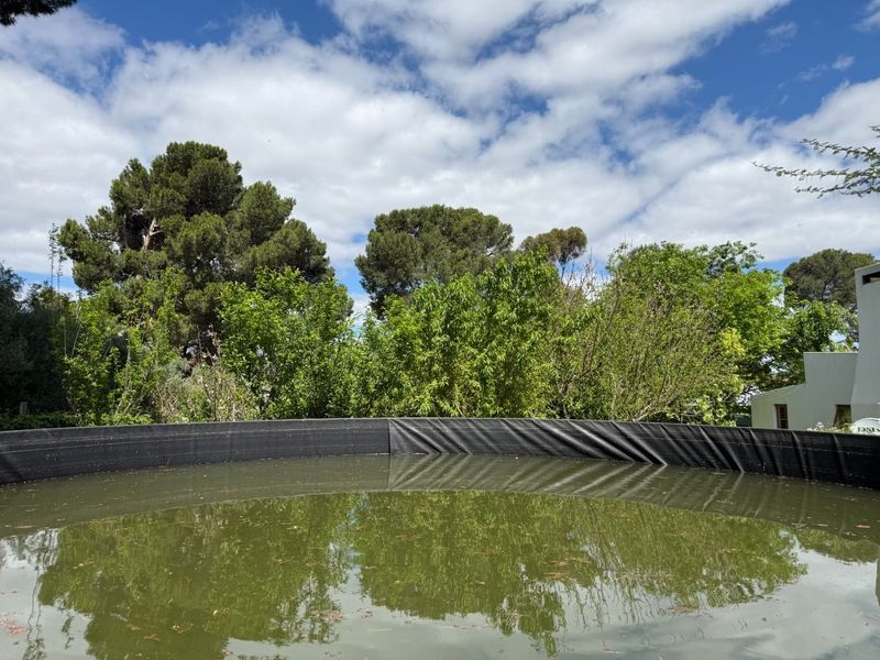A large circular water reservoir or storage tank situated within a garden setting, surrounded by mature trees and greenery.