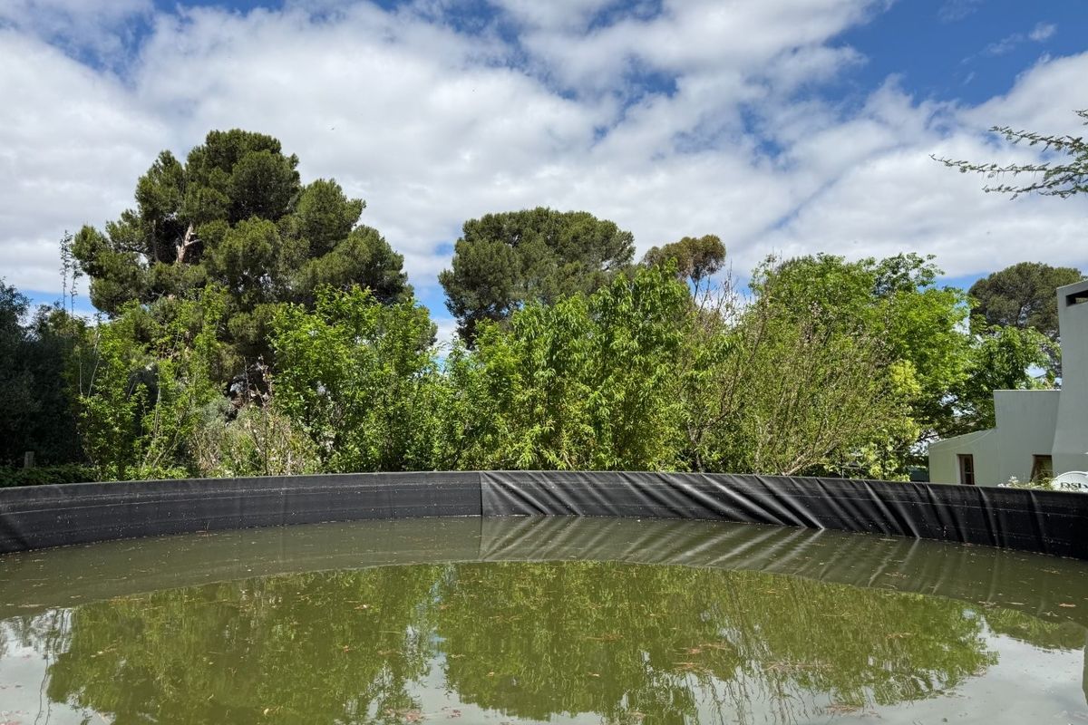 A large circular water reservoir or storage tank situated within a garden setting, surrounded by mature trees and greenery.