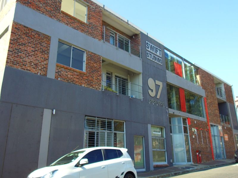 Front exterior view of Swift Studios apartment building featuring exposed brickwork, modern grey accents, and balcony access.