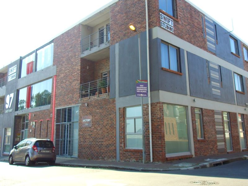 A modern multi-story apartment building featuring a face brick facade, integrated balconies with metal railings, and large windows on a corner street location.