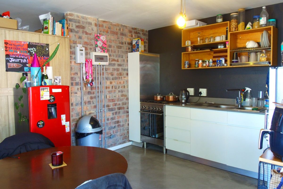 Compact kitchen featuring exposed brick walls, concrete flooring, stainless steel stove, and functional cabinetry with open shelving storage.