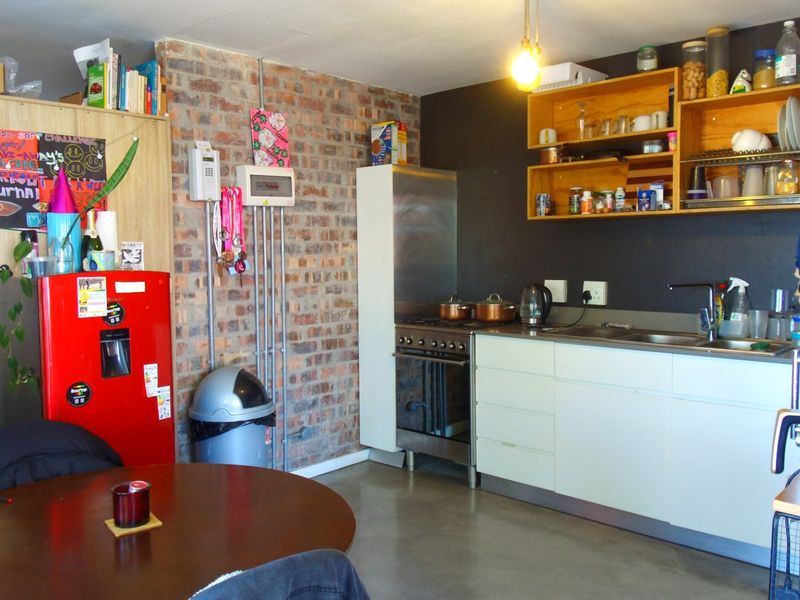 Compact kitchen featuring exposed brick walls, concrete flooring, stainless steel stove, and functional cabinetry with open shelving storage.
