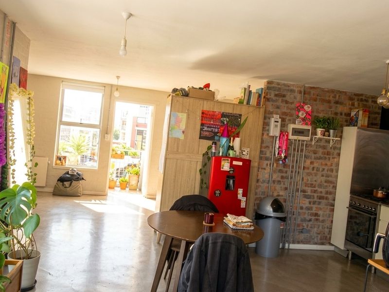Open-plan living area featuring polished concrete floors, an exposed brick feature wall, and a functional kitchen with built-in oven and extractor fan.