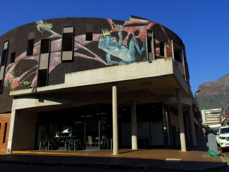 Exterior view of a multi-story apartment building featuring a prominent mural, concrete structural columns, and a paved ground-level entrance area.