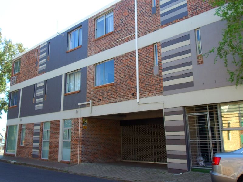 Front elevation of a multi-story apartment building featuring a brick and painted facade with a secure ground-level parking entrance.