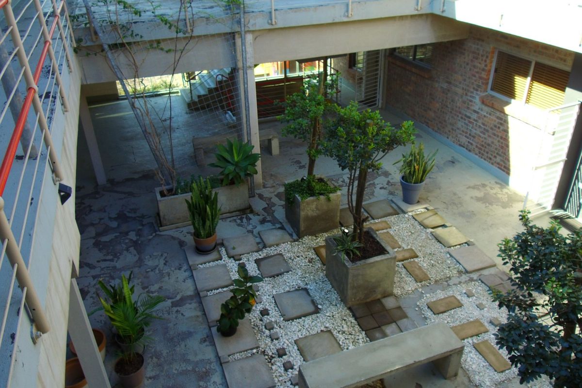 An elevated view of a communal courtyard featuring exposed brick walls, concrete paving, stone landscaping, and a built-in concrete bench.