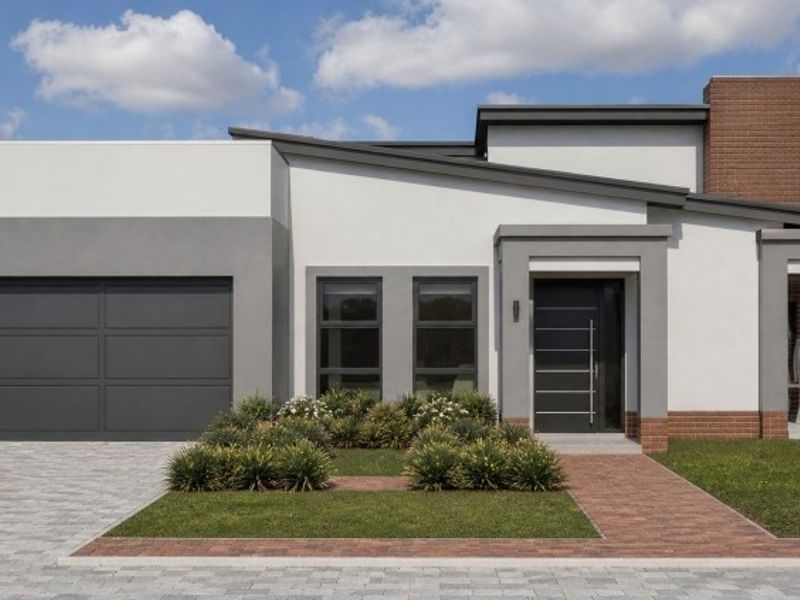 Modern single-story home featuring a double garage, brick chimney detail, paved driveway, and a covered patio entrance with landscaped front garden.