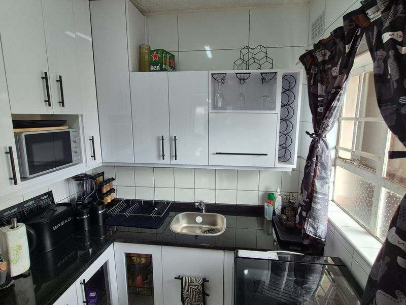 A compact, modern kitchen featuring white high-gloss cabinetry, black granite countertops, and a stainless steel sink with tiled backsplash.