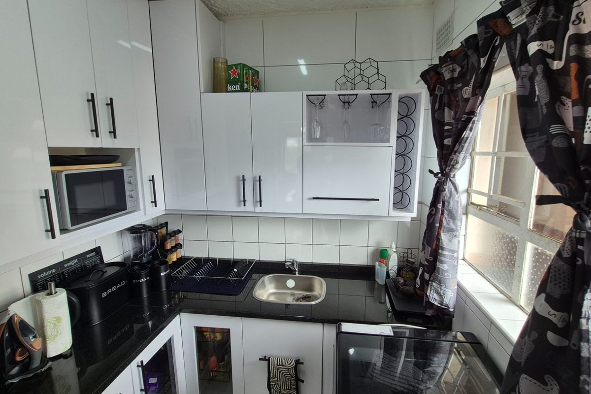 A compact, modern kitchen featuring white high-gloss cabinetry, black granite countertops, and a stainless steel sink with tiled backsplash.