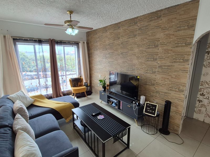 A comfortable living room featuring a textured stone veneer accent wall, tiled flooring, and a ceiling fan, with access to a balcony through sliding doors.