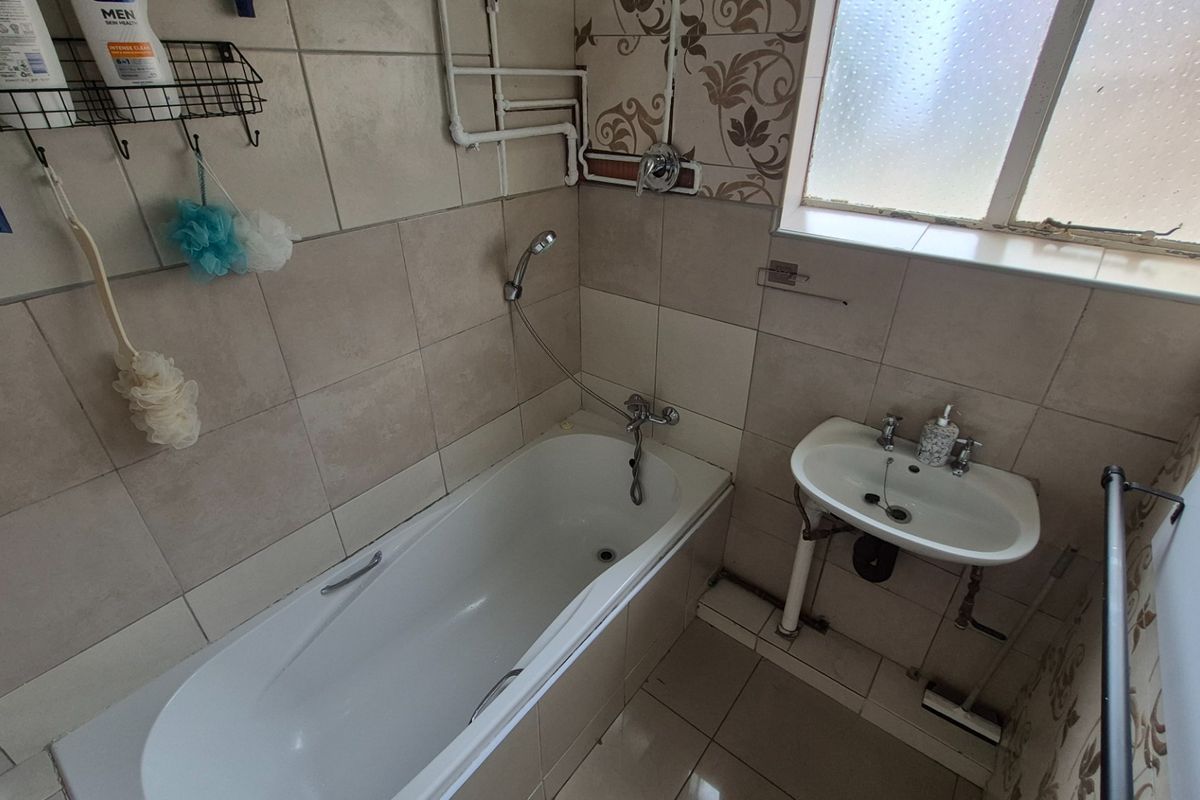 A compact bathroom featuring a bathtub with a handheld shower attachment, a wall-mounted basin, and tiled finishes throughout.