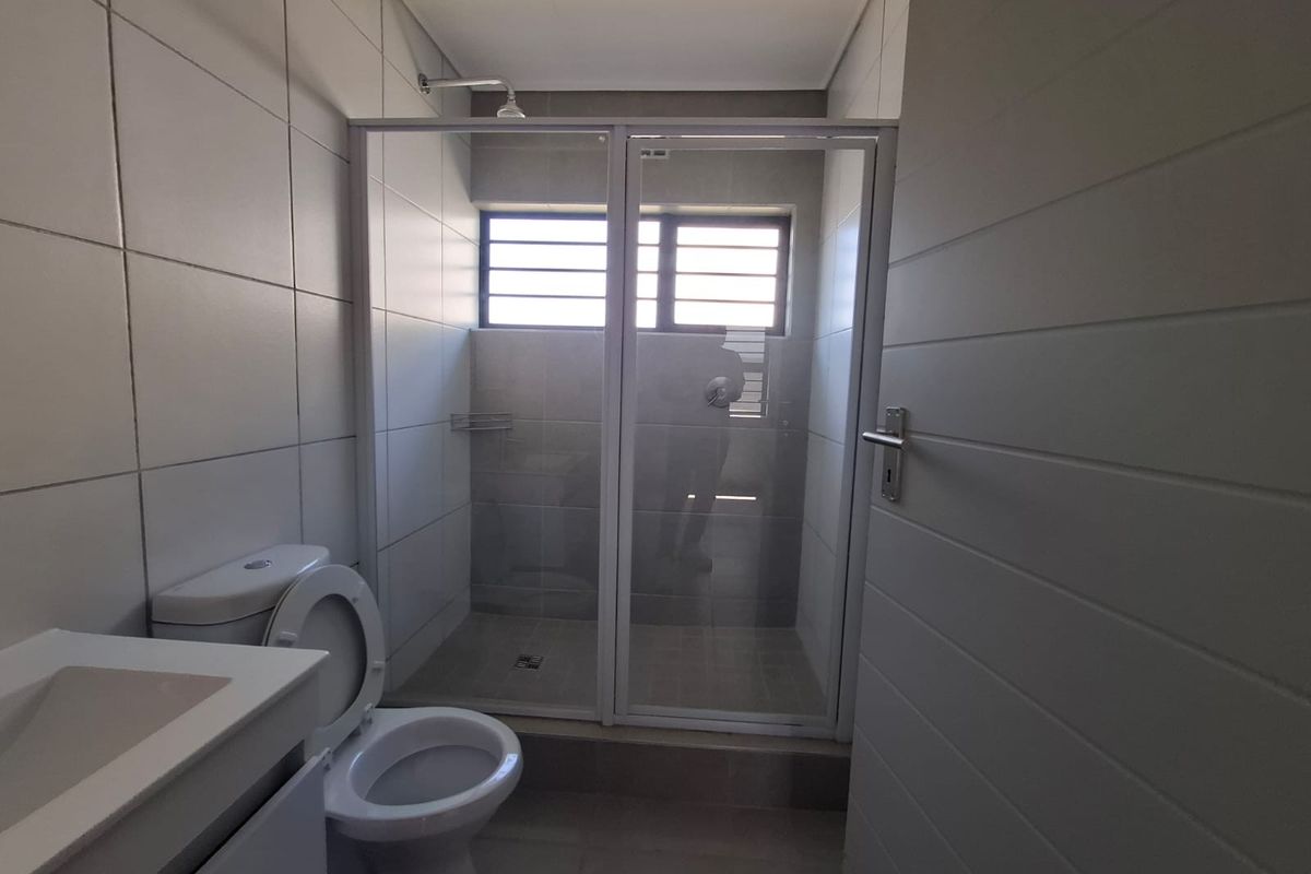 A clean, functional bathroom featuring a glass-enclosed shower, modern toilet, and vanity basin with neutral wall tiling and natural light.