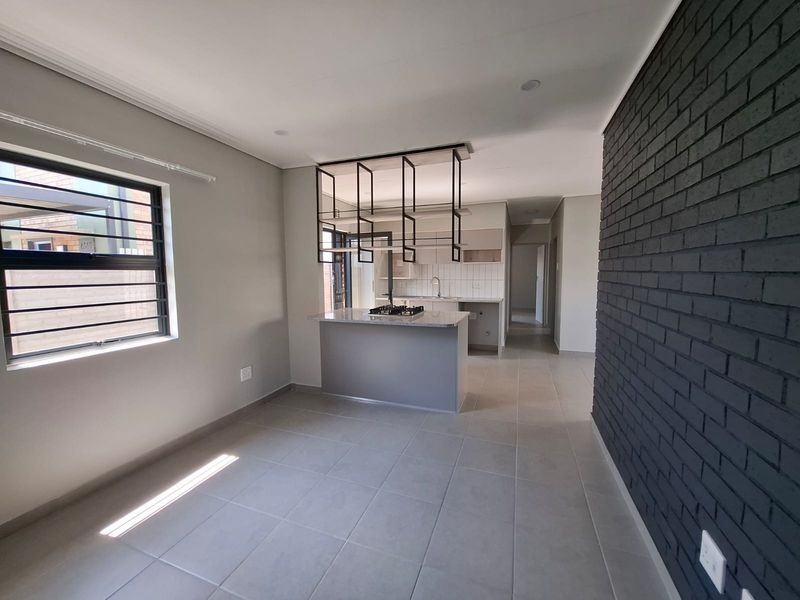 Modern open-plan kitchen featuring a central island with gas hob, suspended shelving, and a striking dark brick feature wall, finished with neutral floor tiles.