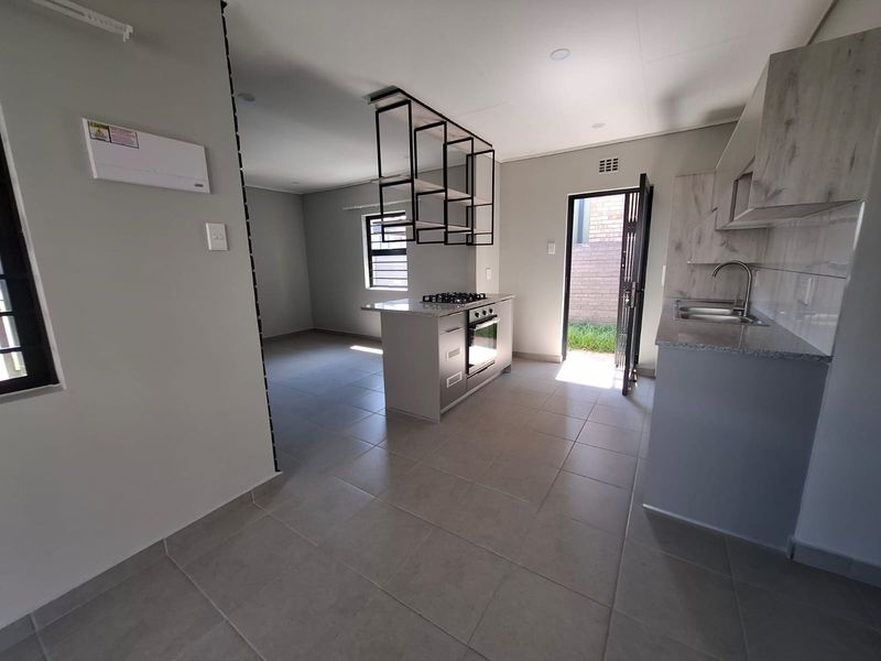 Modern open-plan kitchen featuring a central island with gas hob, built-in oven, suspended shelving, and direct access to the rear exterior.