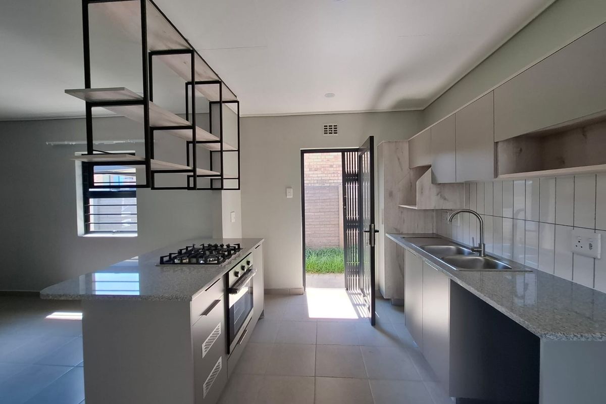 Modern kitchen featuring granite countertops, built-in gas hob, oven, double sink, and unique suspended shelving, leading to an exterior courtyard.