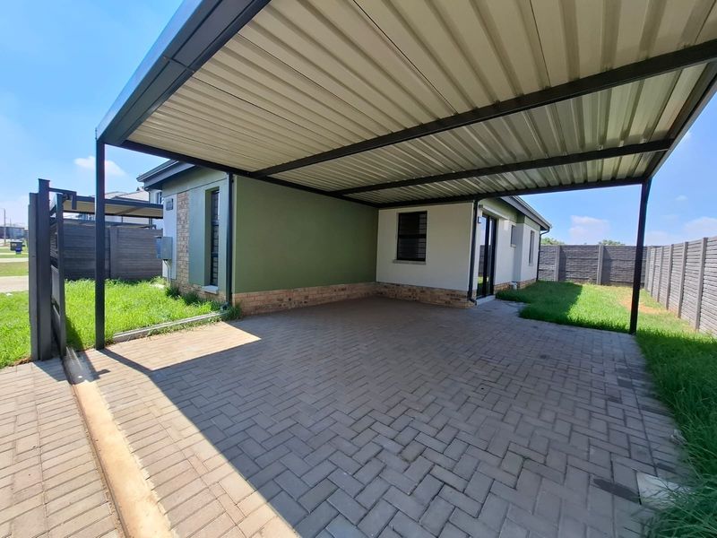 A spacious paved carport area providing covered parking, featuring a sturdy metal roof structure and enclosed by brick boundary walls.